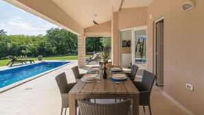 A poolside dining area with a table set for four, surrounded by wicker chairs, overlooking a swimming pool and a garden. - Lovely apartment in Labin with sauna (Labin)