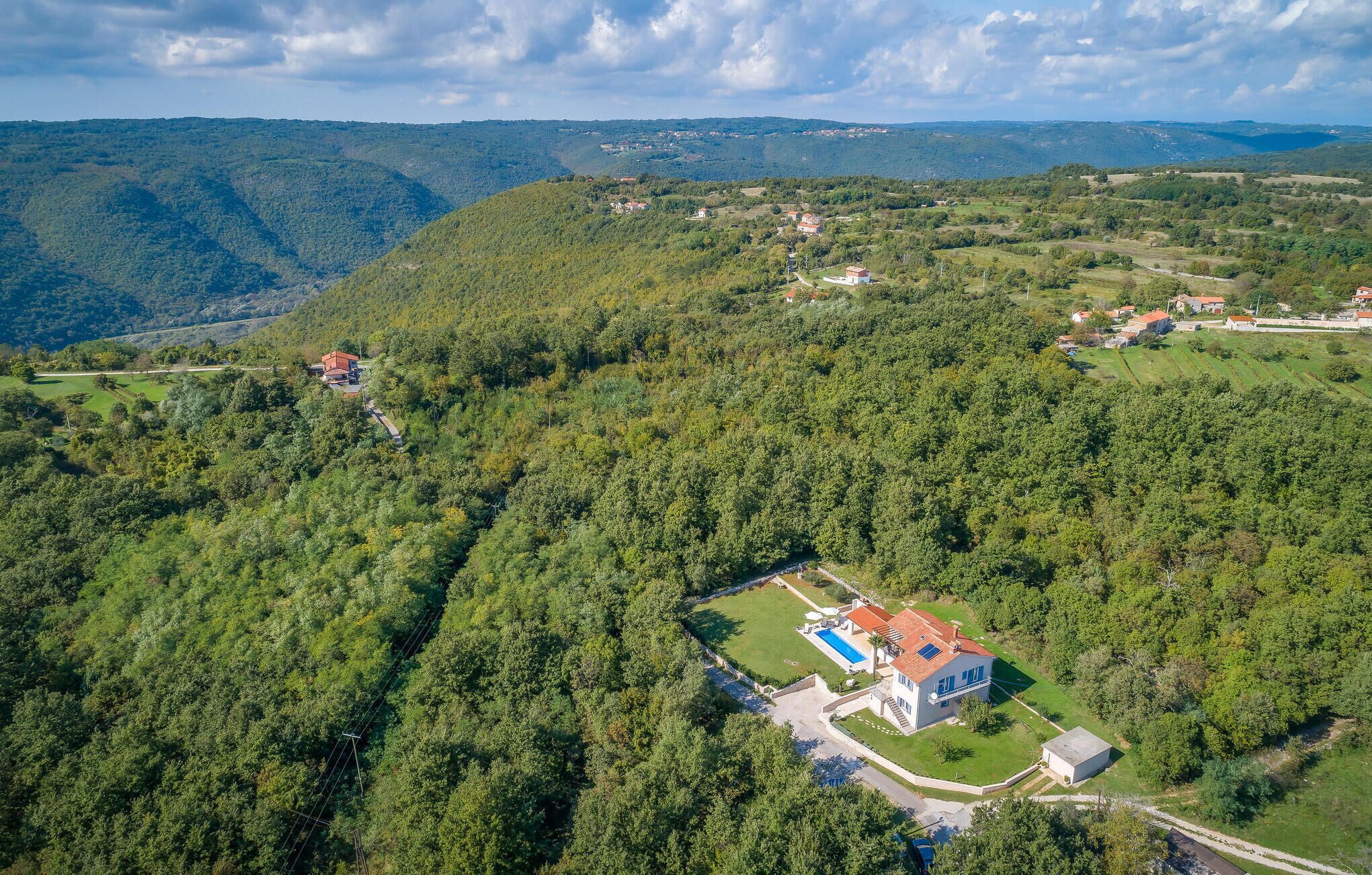 Luftaufnahme eines Anwesens mit Schwimmbad, großem Haus und bewaldeten Hügeln ringsum.