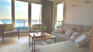 A spacious room with a large bed, two armchairs, a coffee table, and a view of the sea through large windows. - Refugium Strandallee - Refugium Strandallee, 91 m², 2 - 4 persons (Neustadt in Holstein)