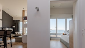 A modern living room with a sofa, a dining table, and a view of the sea through large windows. - Refugium Strandallee - Refugium Strandallee, 91 m², 2 - 4 persons (Neustadt in Holstein)