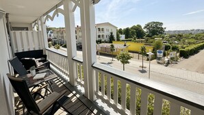Un balcone con tavolo e sedie, affacciato su una strada con edifici e vegetazione.