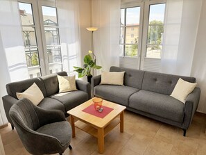 A modern living room with a grey sofa, two armchairs, a wooden coffee table, and a floor lamp. - MR: Villa Annika Whg. 07 with south-facing balcony - Villa Annika Whg. 07 with south-facing balcony (Sellin)