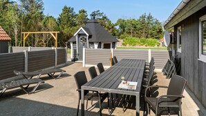 En udendørs terrasse med et bord og stole, en lille pergola og et træhegn.