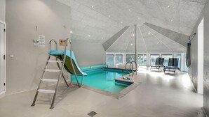 En rummelig indendørs swimmingpool med vandrutsjebane, stige og liggestole.