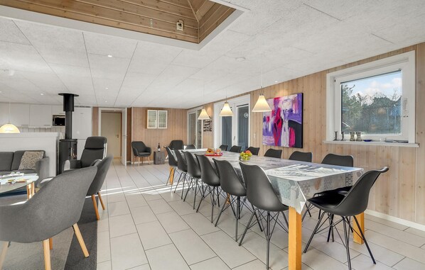A modern dining area with a long table, black chairs, and a wooden accent wall. - Cozy home in Ringkøbing with sauna (Ringkøbing)