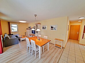 Un salon comprenant un canapé, une table à manger avec des chaises, un téléviseur et un coin cuisine avec des placards et une fenêtre.