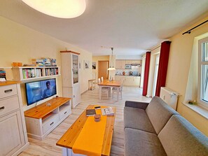 Un salon avec un téléviseur, un canapé, une table à manger et une cuisine à l’arrière-plan.
