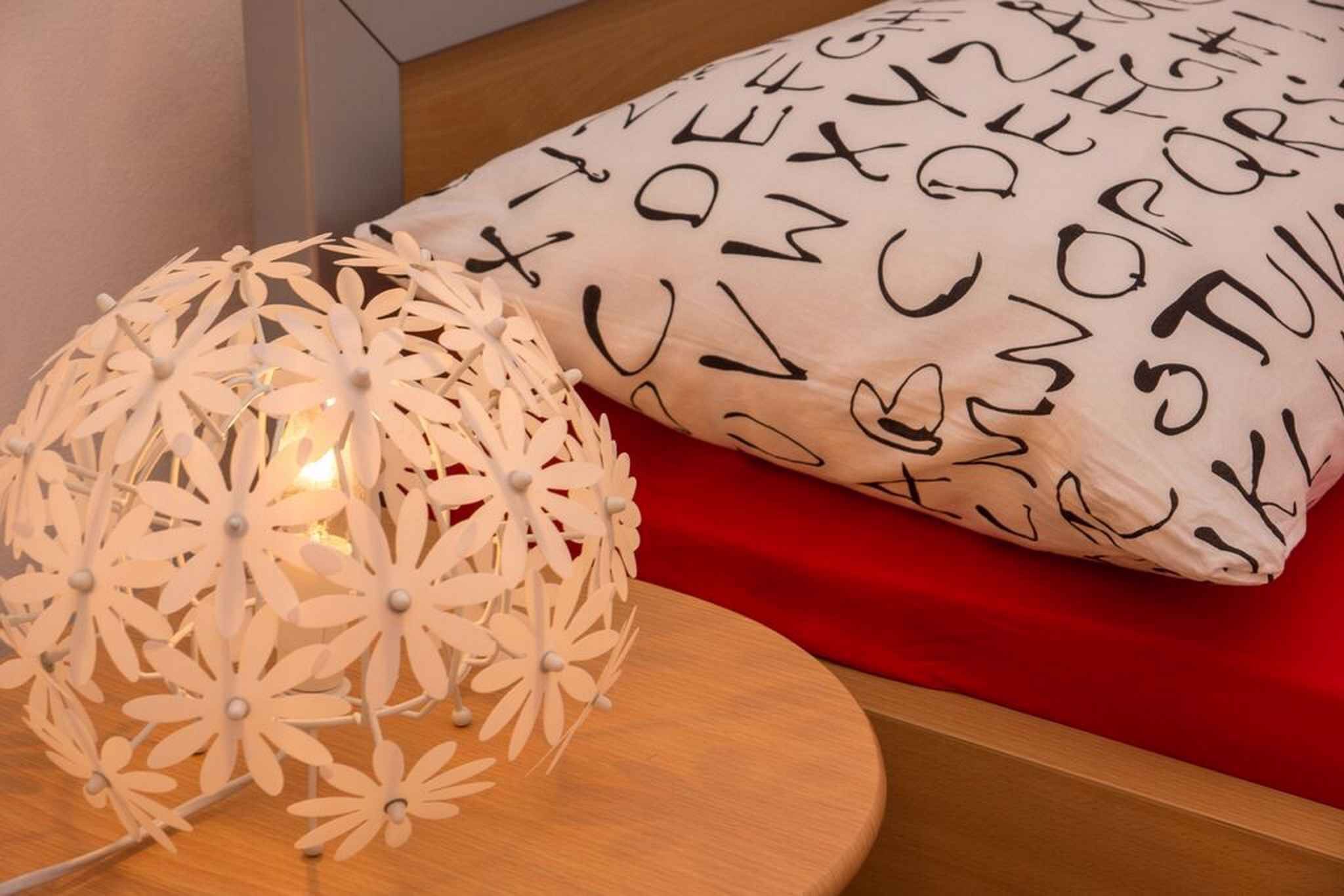A decorative white spherical light fixture with a floral design, a red cushion with black text, and a wooden surface.