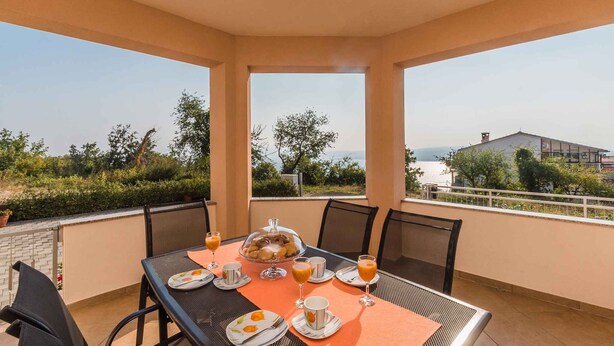 A covered outdoor dining area with a table set for breakfast, overlooking a scenic landscape.