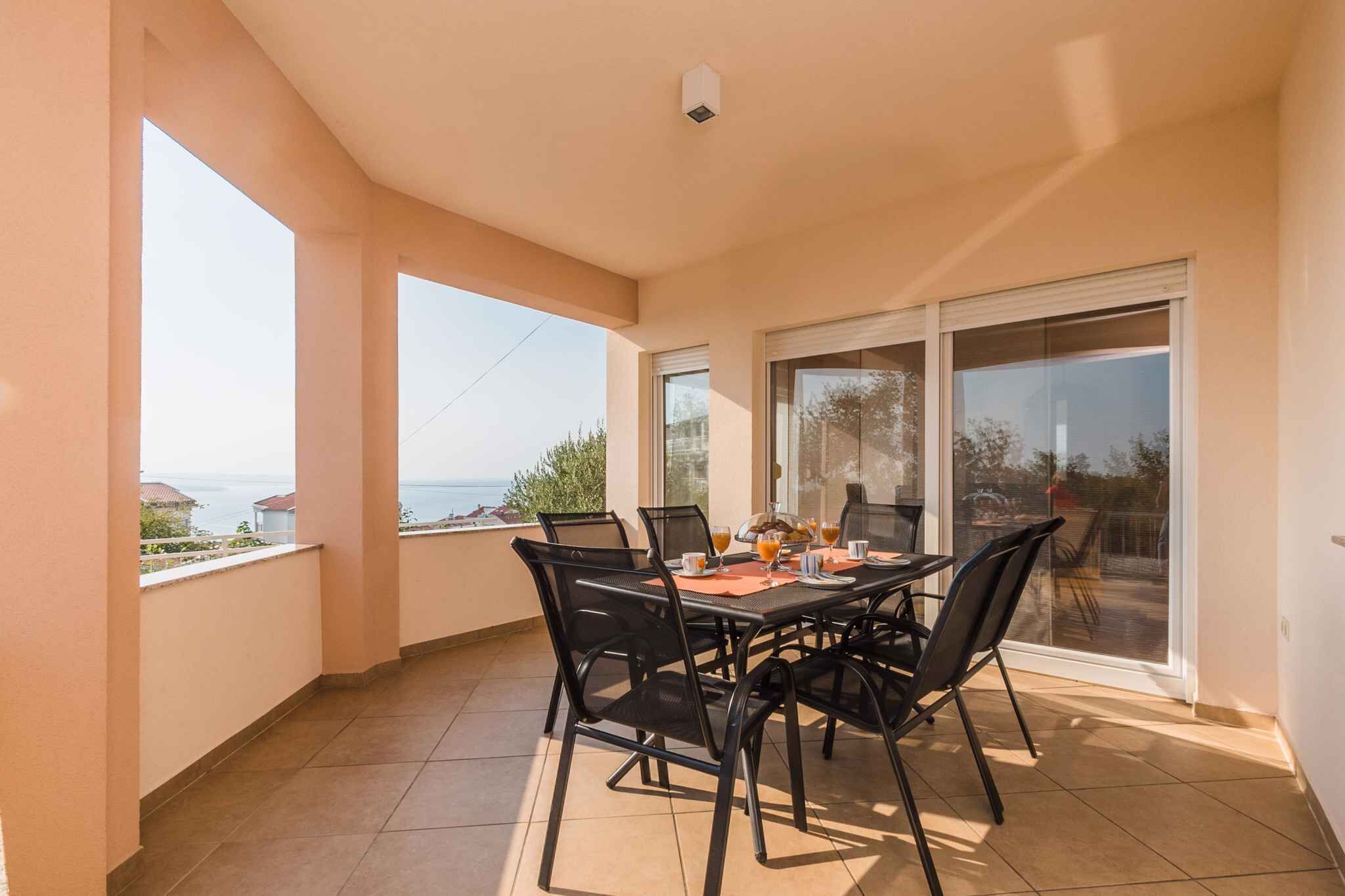 Een balkon met een tafel voor twee, grote ramen en uitzicht op zee.