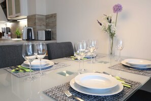A dining table set with white plates, clear wine glasses, and silverware on patterned placemats.
