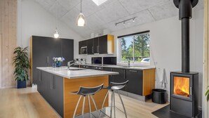 A modern kitchen with a central island, bar stools, a stove, and a large window.