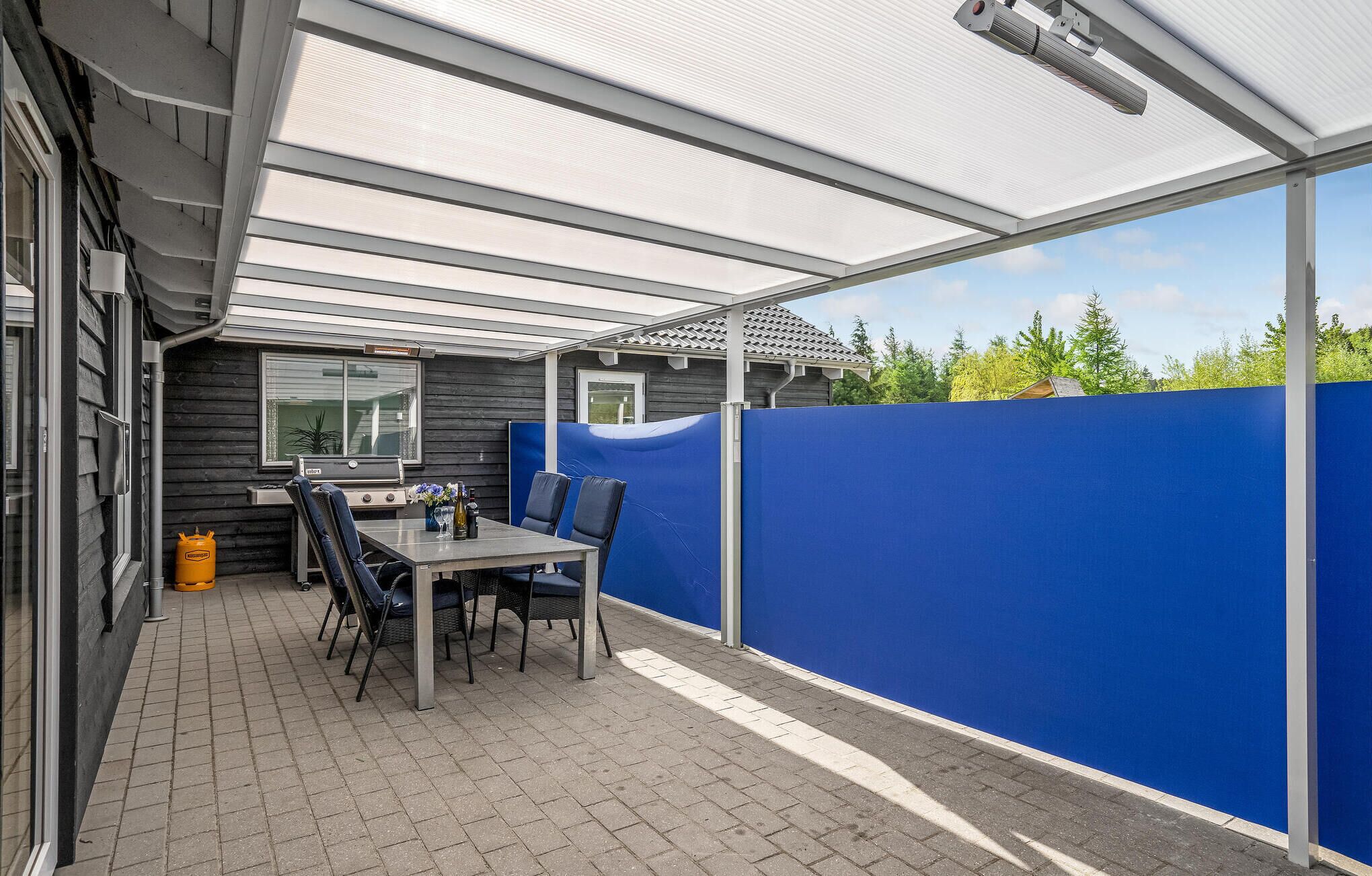 An outdoor patio with a table and chairs, a grill, and a blue privacy screen.