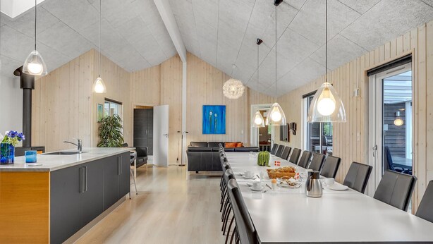 A modern kitchen with a central island, a dining area with a long table and chairs, and a cozy seating area with a sofa and a coffee table.