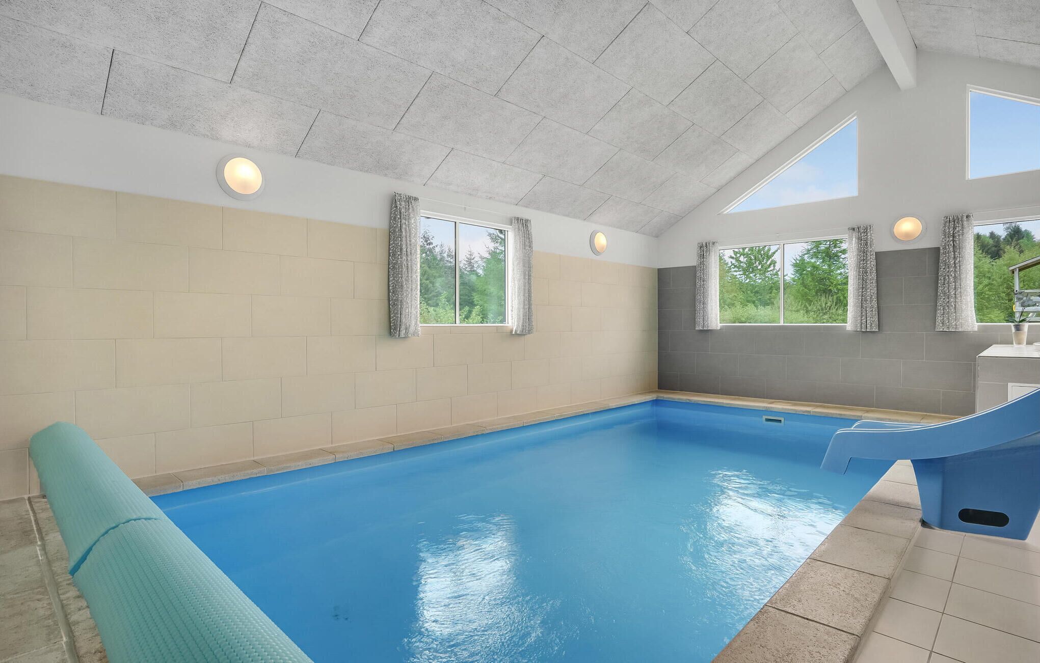 Piscina interna con pavimento blu, pareti color beige e finestre con tende.