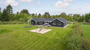 A modern house with a large backyard, including a trampoline and play structure.