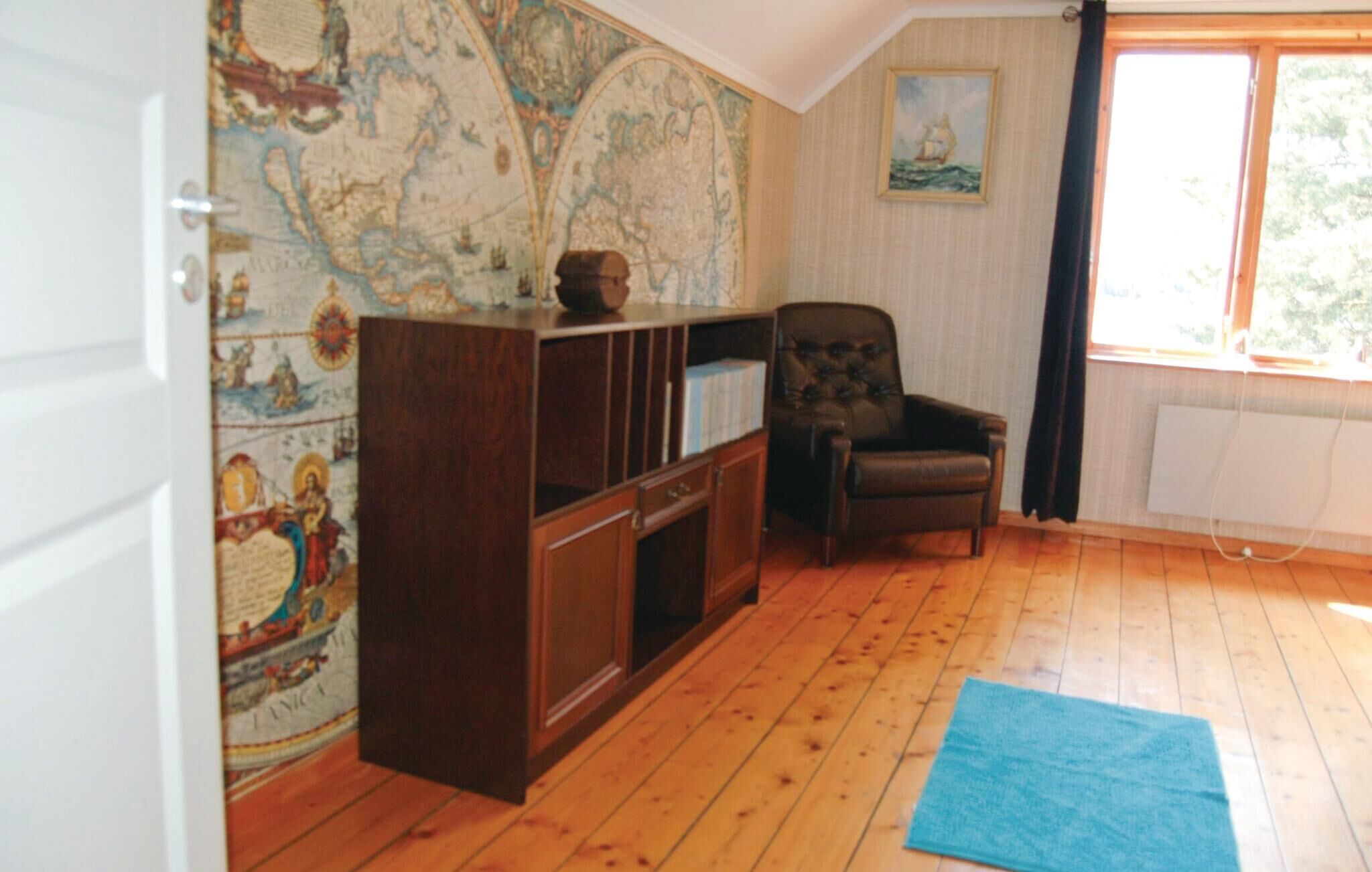 Une pièce avec un plancher en bois, un fauteuil en cuir foncé, une armoire en bois et une grande carte accrochée au mur.