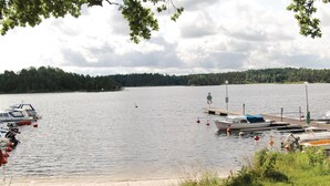 A lakeside dock with several boats moored, a sandy shore, and a forested background. - 2 bedroom beautiful home in åsensbruk (Åsensbruk)