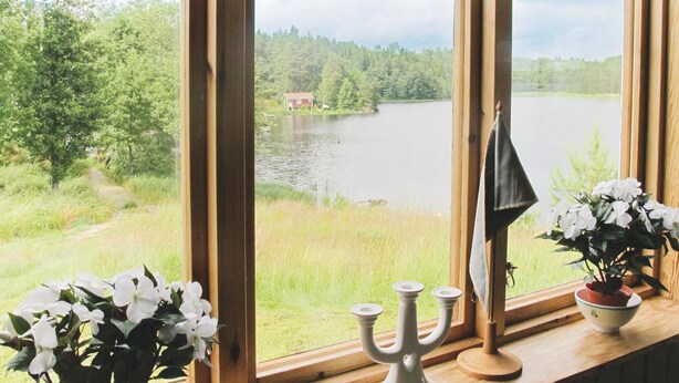 A window with a view of a lake and trees, a candelabra, and a potted plant. - 2 bedroom beautiful home in åsensbruk (Åsensbruk)