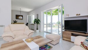 Una sala de estar moderna con sofá, mesa de centro y televisor. Se aprecia una ventana grande con vistas a zonas verdes.