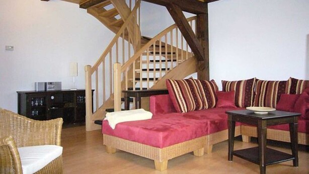 Un salon chaleureux avec un escalier en bois, des meubles en osier et une table basse en bois foncé.
