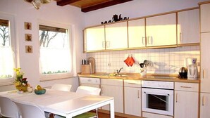 Une cuisine compacte avec des meubles blancs, un four encastré et un coin repas comprenant une table et des chaises.