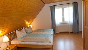 Une chambre avec un plafond en bois, un lit avec une literie blanche, une table de chevet avec une lampe et une fenêtre avec des rideaux.
