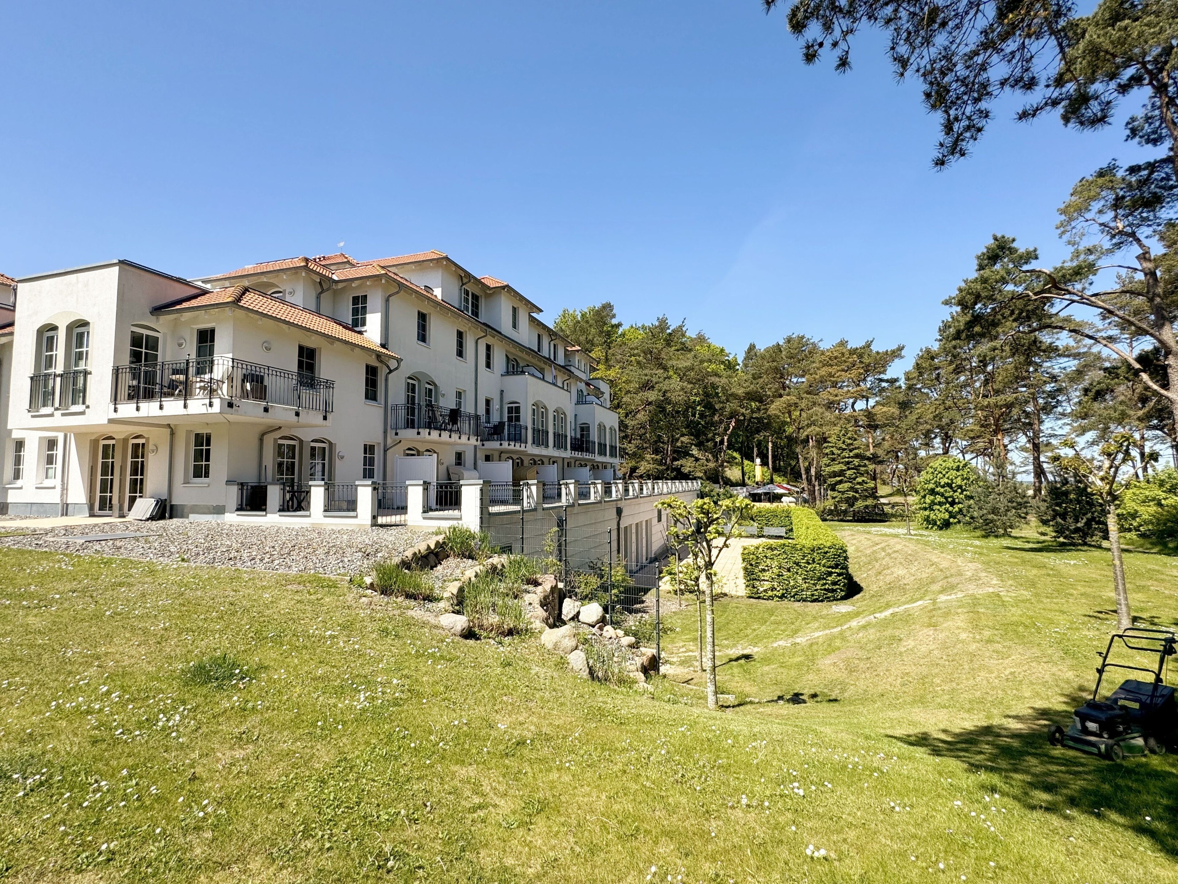 Un grande edificio a più piani con balconi, un prato curato e alberi circostanti.