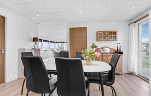 Ein Essbereich mit einem runden Tisch, schwarzen Stühlen und einer Vase mit Blumen. Es gibt einen Holzschrank mit Glastüren und einen Spiegel darüber.