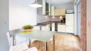 A compact kitchen with a glass dining table, white chairs, and a potted plant.