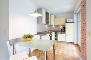 A compact kitchen with a glass dining table, white chairs, and a potted plant.