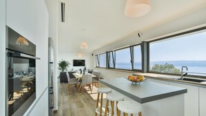 Una cocina moderna con una isla grande, taburetes de bar y una zona de comedor con vistas al mar.