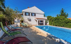 A two-story house with a swimming pool, outdoor seating, and a garden.
