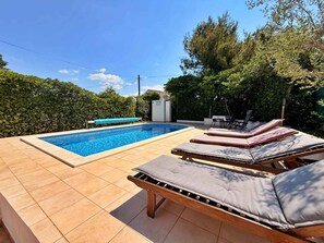 A swimming pool with lounge chairs and a tiled deck. - Holiday apartment with shared pool and barbecue (Šilo)
