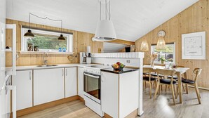 A modern kitchen with white cabinetry, a built-in oven, and a dining area with wooden chairs and a white table. - Cozy home in Oksbøl with sauna (Oksbøl)