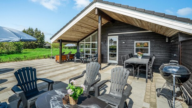 An outdoor patio with wooden furniture, a grill, and a covered seating area. - Cozy home in Oksbøl with sauna (Oksbøl)