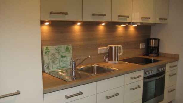A modern kitchen with white cabinets, stainless steel appliances, a coffee maker, and a kettle. - 002 re (BC 3) - BUE - House Stüven (Büsum)