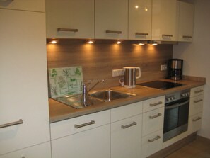 A modern kitchen with white cabinets, stainless steel appliances, a coffee maker, and a kettle. - 002 re (BC 3) - BUE - House Stüven (Büsum)