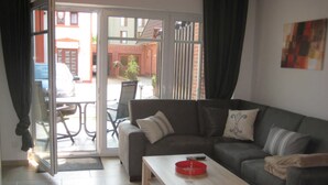 A living room with a sofa, a coffee table, and a sliding glass door leading to an outdoor area. - 002 re (BC 3) - BUE - House Stüven (Büsum)