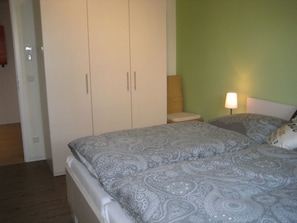 A bedroom with a bed, a nightstand, a lamp, and a wardrobe. - 002 re (BC 3) - BUE - House Stüven (Büsum)