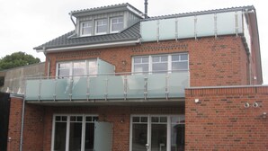 A two-story building with a glass balcony, brick facade, and large glass doors. - 002 re (BC 3) - BUE - House Stüven (Büsum)