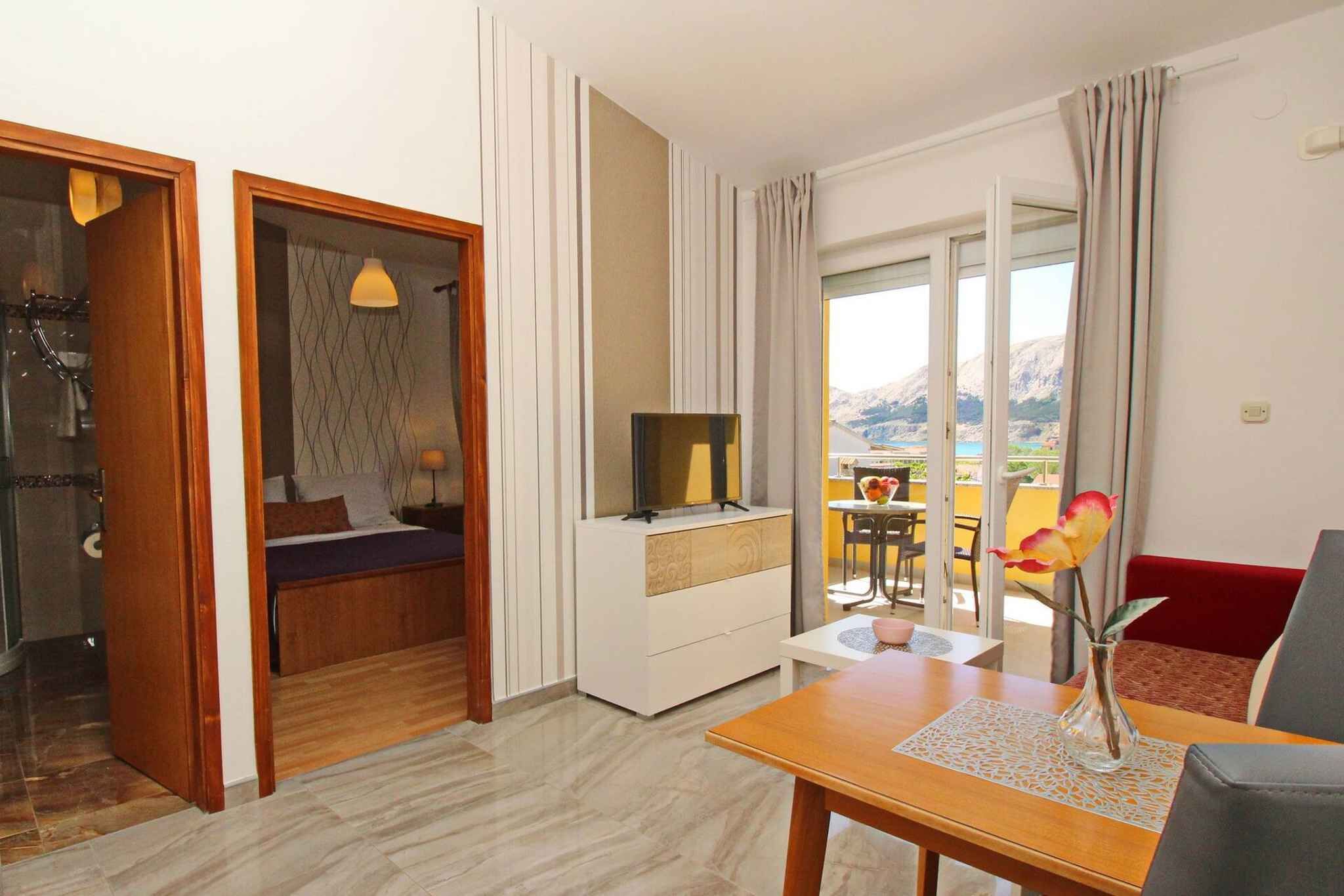 A hotel room with a bed, a TV on a white cabinet, a dining table with a vase of flowers, and a view of the mountains through the window.