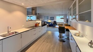 A modern kitchen with a central island, a dining area with a wooden table, and a view of the sea through large windows. - Gorgeous home in Thisted with sauna (Thisted)