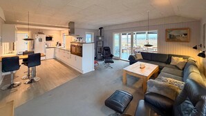 A spacious living area with a sofa, coffee table, and a dining area with chairs and a kitchen in the background. - Gorgeous home in Thisted with sauna (Thisted)