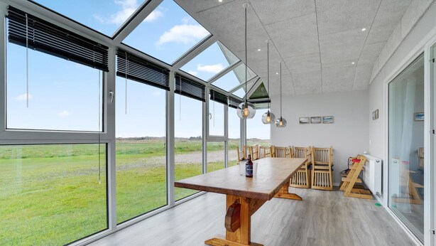 A modern dining area with a large table, wooden chairs, and large windows offering a view of a grassy field. - Gorgeous home in Thisted with sauna (Thisted)