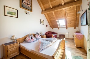 Un dormitorio con techo de madera, una cama con ropa de cama estampada, una mesita de noche, un aparador y una ventana.