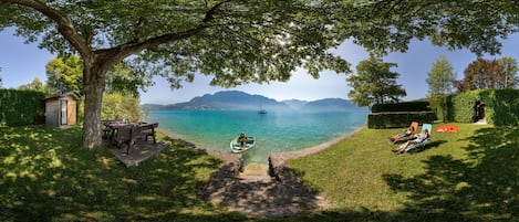 A lakeside view with a dock, a boat, and a picnic table under a tree.