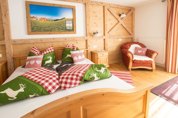 Une pièce chaleureuse avec un lit doté d’une literie à carreaux, d’une tête de lit en bois, d’un fauteuil rouge, d’une petite table de chevet en bois et d’une lampe fixée au mur.