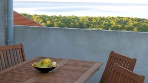 Un tavolo di legno con una ciotola di frutta, due sedie con cuscini a righe e vista su un paesaggio verde.