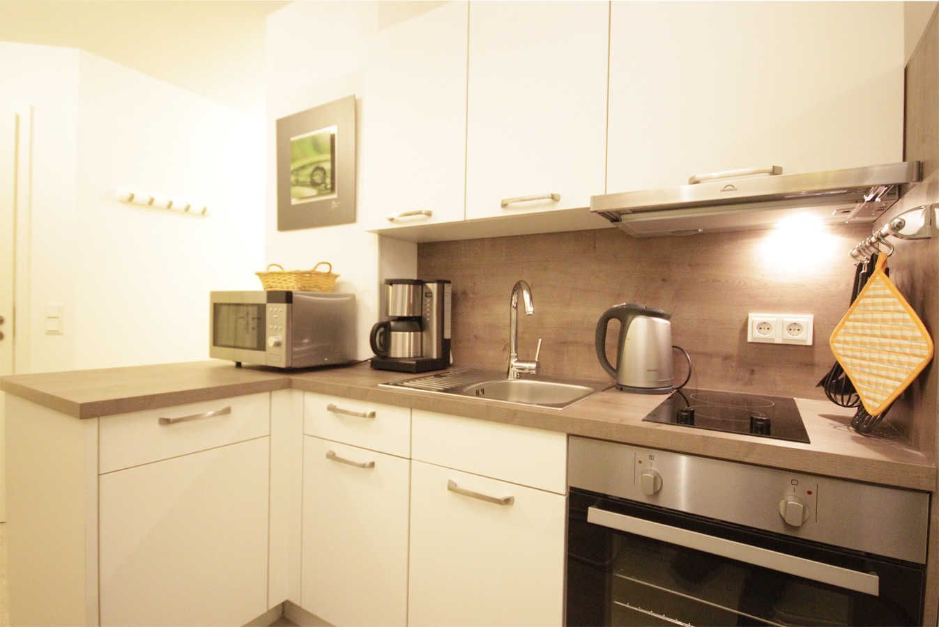 A compact kitchen with a microwave, coffee maker, kettle, and oven.